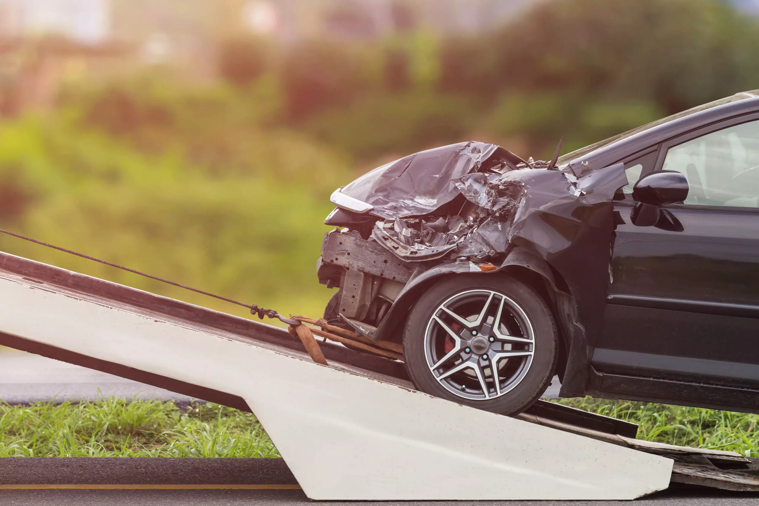 Un'auto nera gravemente danneggiata viene trasportata su un carro attrezzi, mostrando l'impatto frontale.